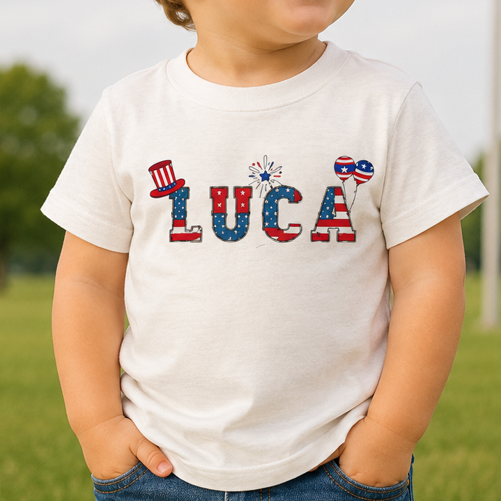 Child wearing a white t-shirt with 'LUCA' printed in colorful letters, standing in a field with an American flag in the background.