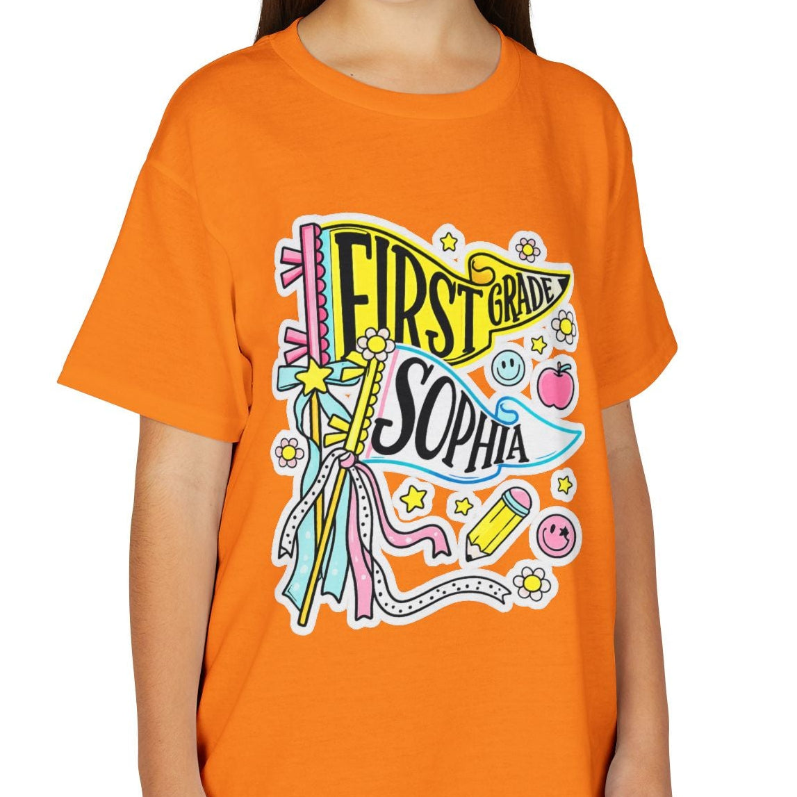 A young girl with long brown hair smiling, wearing a bright orange short-sleeve t-shirt with a colorful 'First Born Sophia' graphic on the front, paired with khaki cargo pants, against a plain white background.