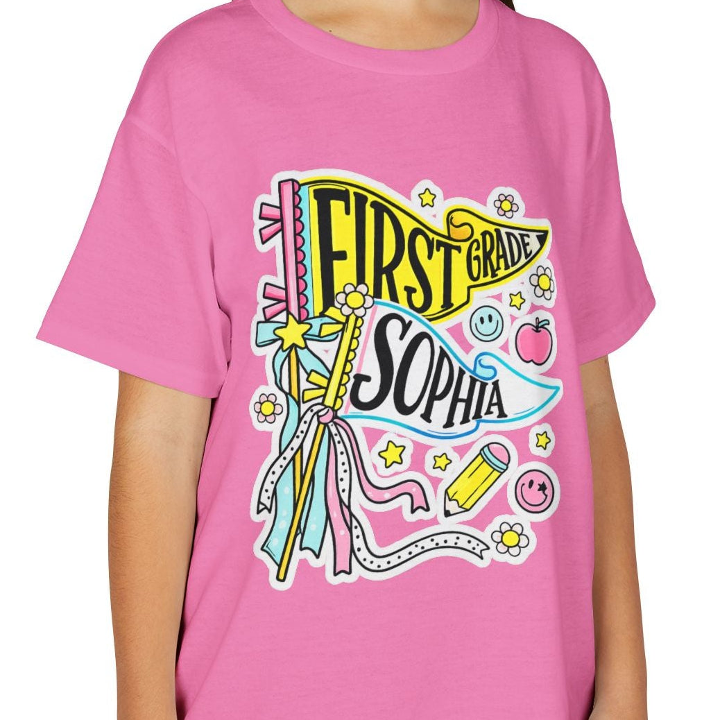 A young girl smiling while wearing a bright pink t-shirt with a colorful 'First Banana Sophia' graphic on the front, paired with khaki cargo pants, set against a plain white background.