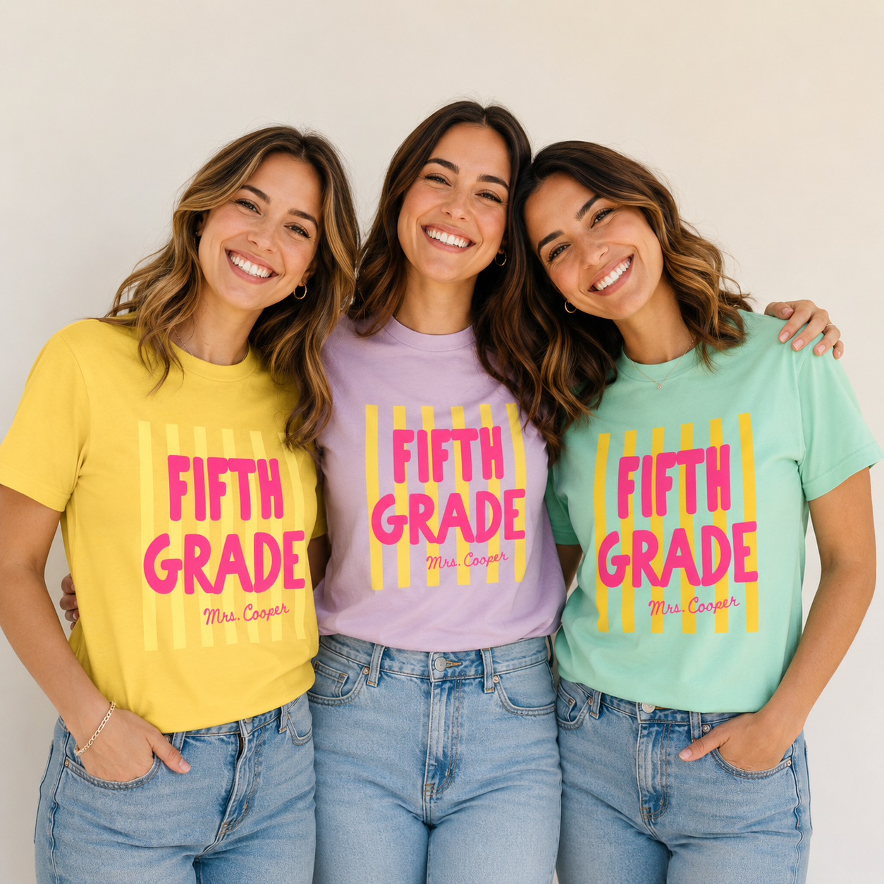Three women wearing personalized striped grade teacher tees in yellow, lilac and mint
