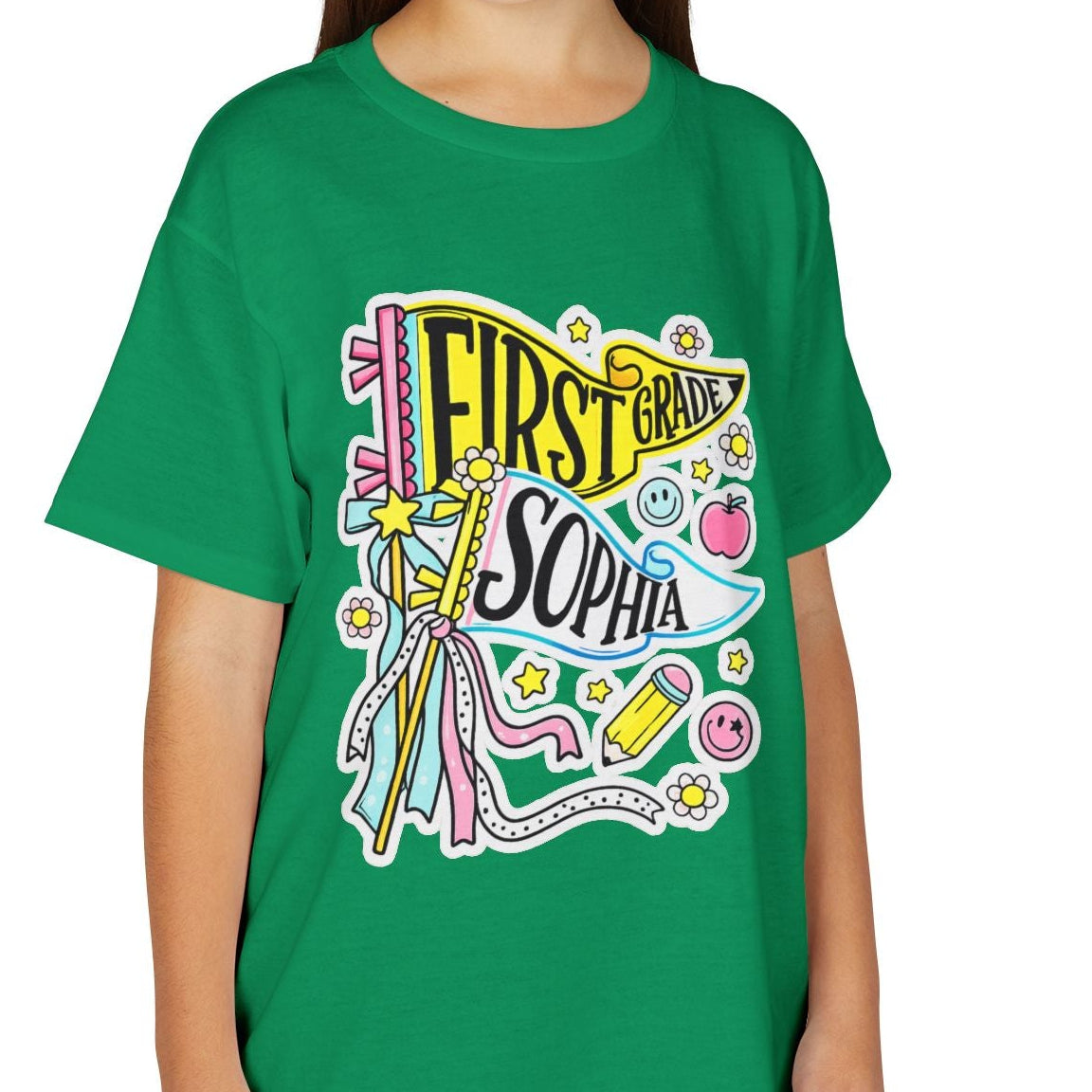 A young girl with long brown hair smiling, wearing a bright green short-sleeve t-shirt with a colorful 'First Year Sophomore' graphic on the front, paired with khaki cargo pants, against a plain white background.