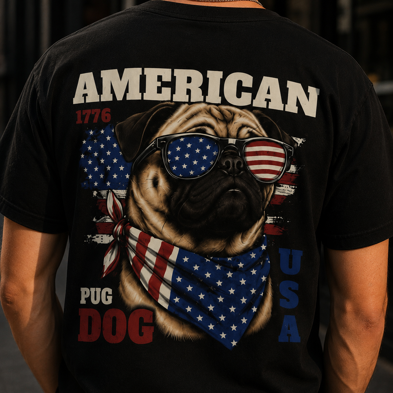 Black t-shirt with a pug dog graphic wearing American flag sunglasses and bandana, text 'American Pug Dog USA' on a dark background.