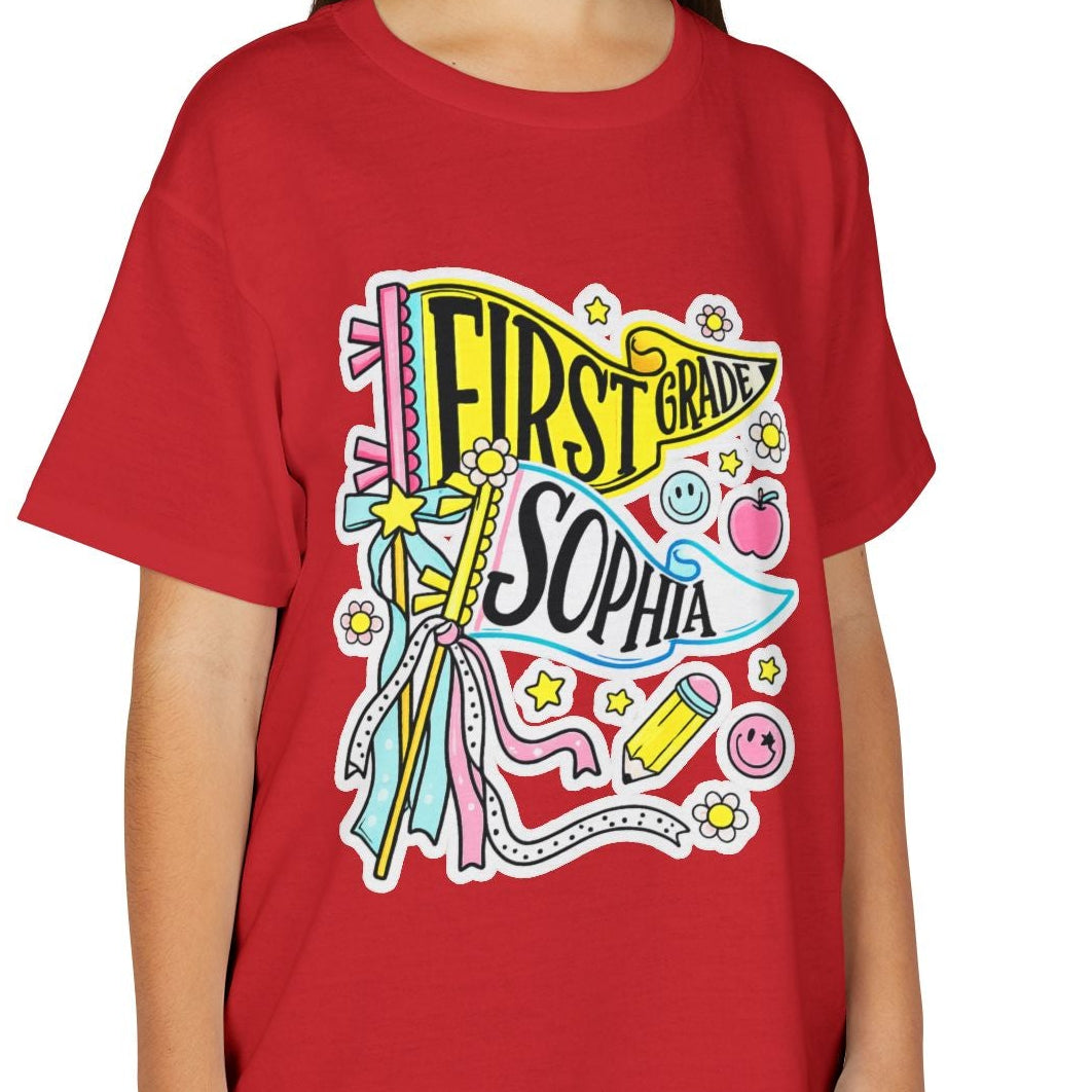 A young girl with long brown hair smiling while wearing a red short-sleeve graphic t-shirt with a colorful 'First Born Sophia' design, paired with khaki cargo pants, against a plain white background.