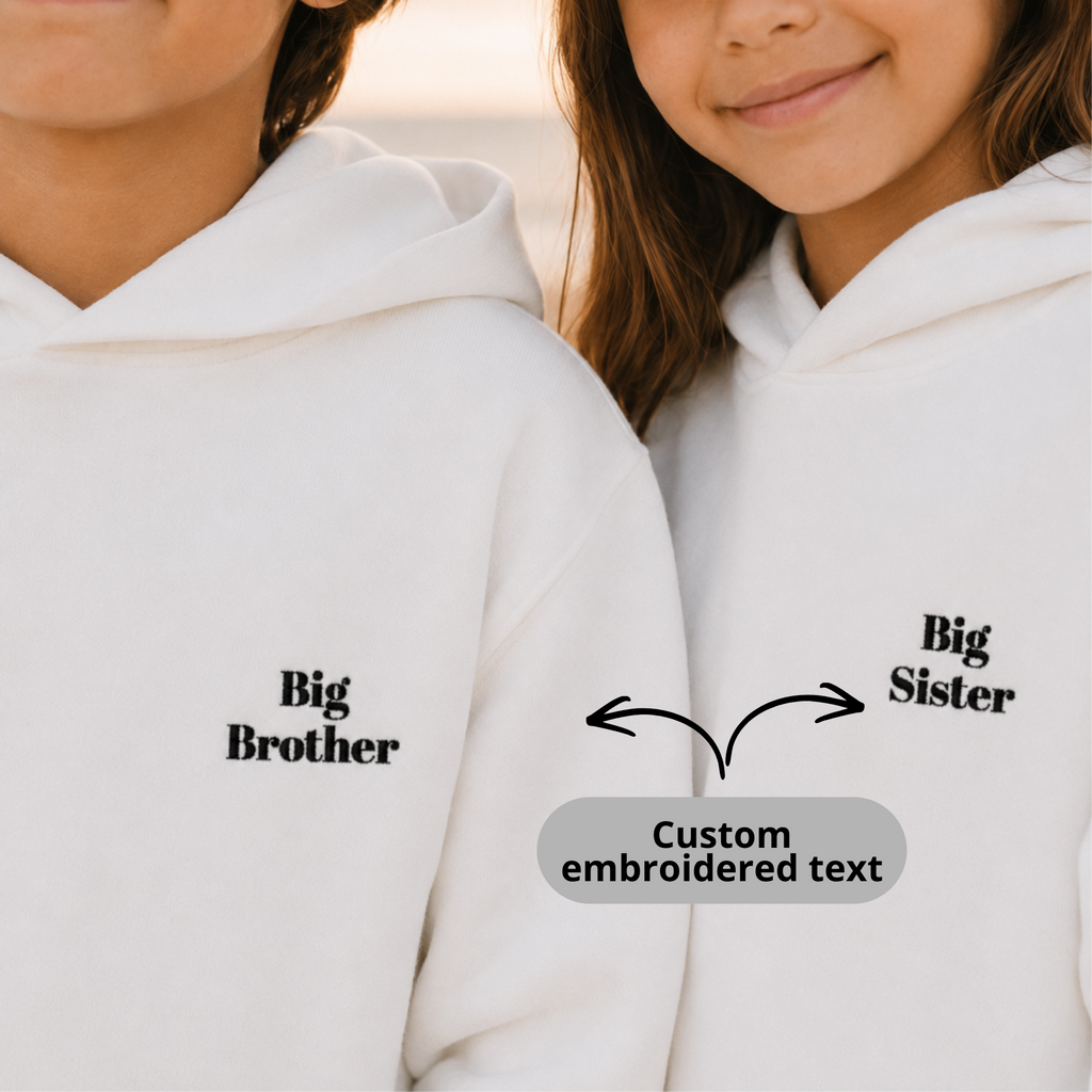 Two children wearing white hoodies with 'Big Brother' and 'Big Sister' text on a plain background.
