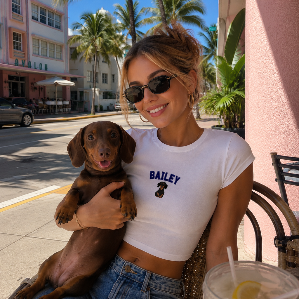 Woman holding a dog on a city street with palm trees and buildings in the background