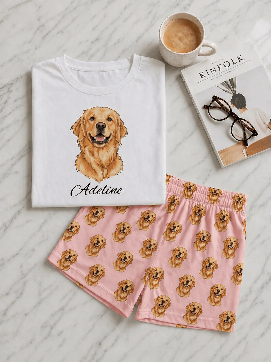 White t-shirt with a dog illustration and pink shorts with dog pattern on a light wooden surface.