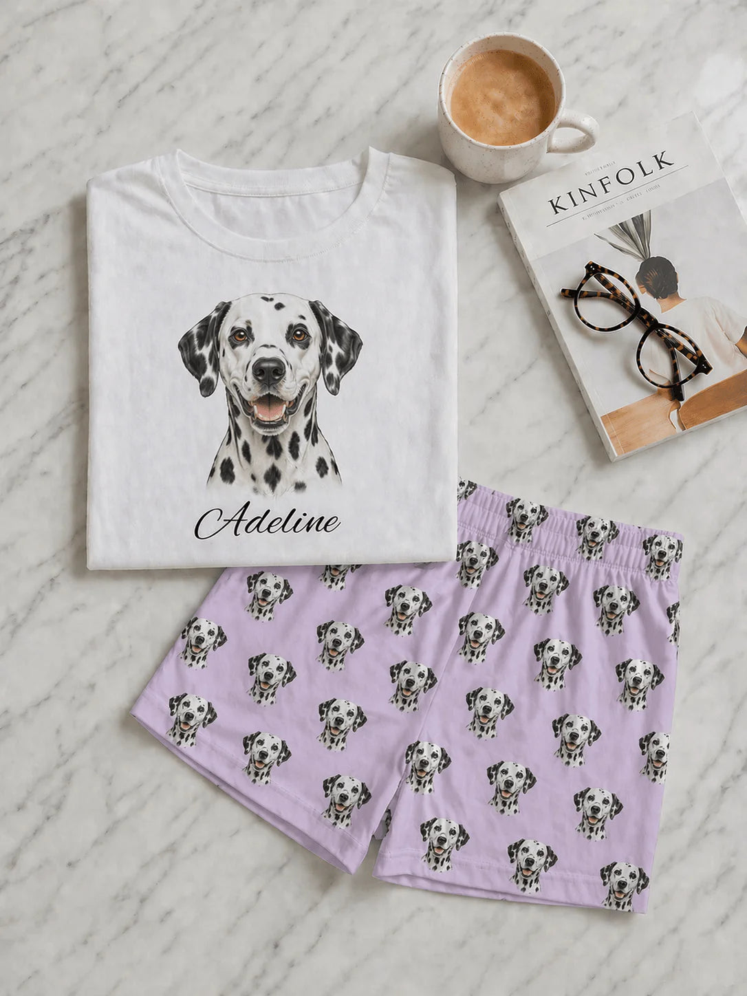 White t-shirt with Dalmatian illustration and purple shorts with Dalmatian pattern on a textured surface.