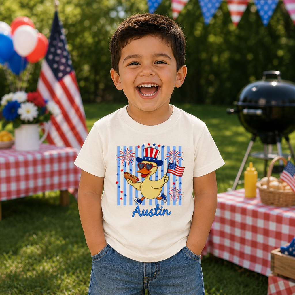 Child wearing a t-shirt with a patriotic duck design in an outdoor setting with American flags and balloons.