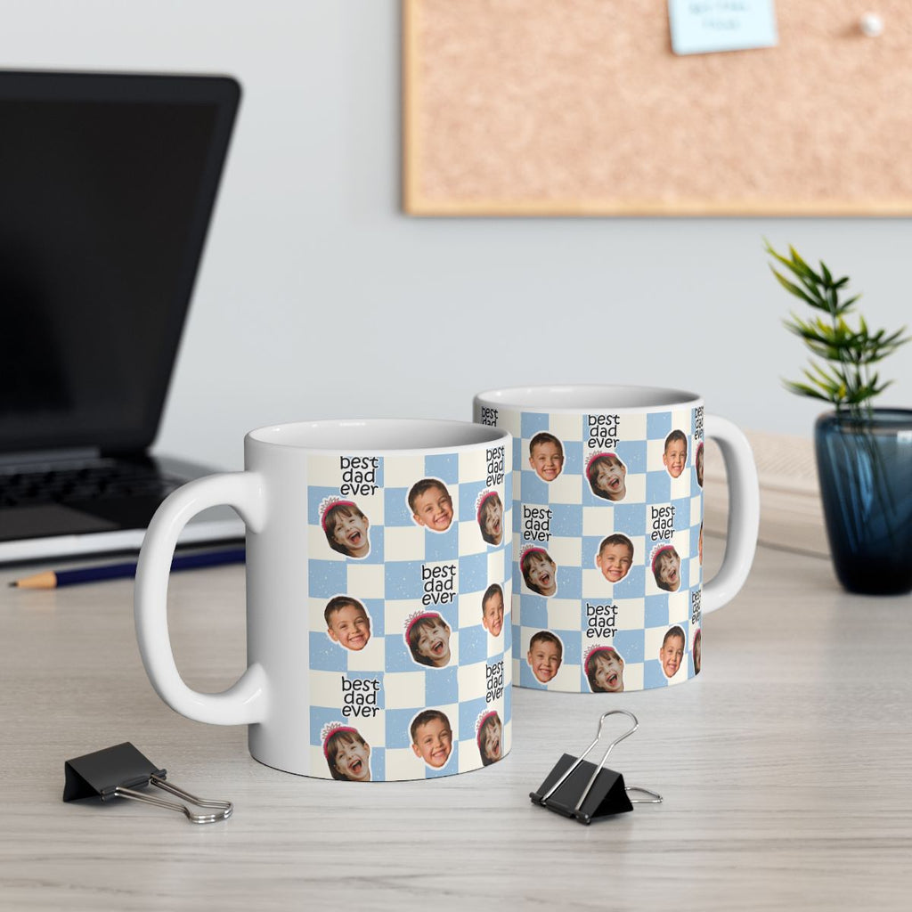 Two white mugs with black pattern on a desk with office supplies and a plant.