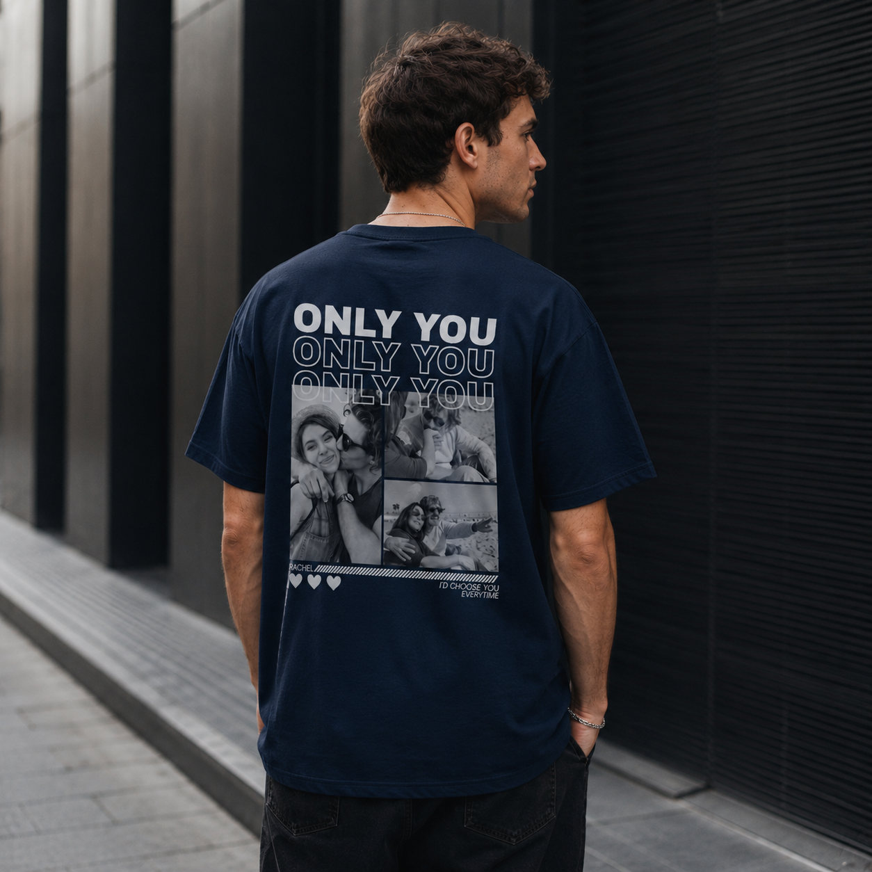 Man wearing a navy blue t-shirt with a collage design and text 'ONLY YOU' on the back, standing against a dark wall.