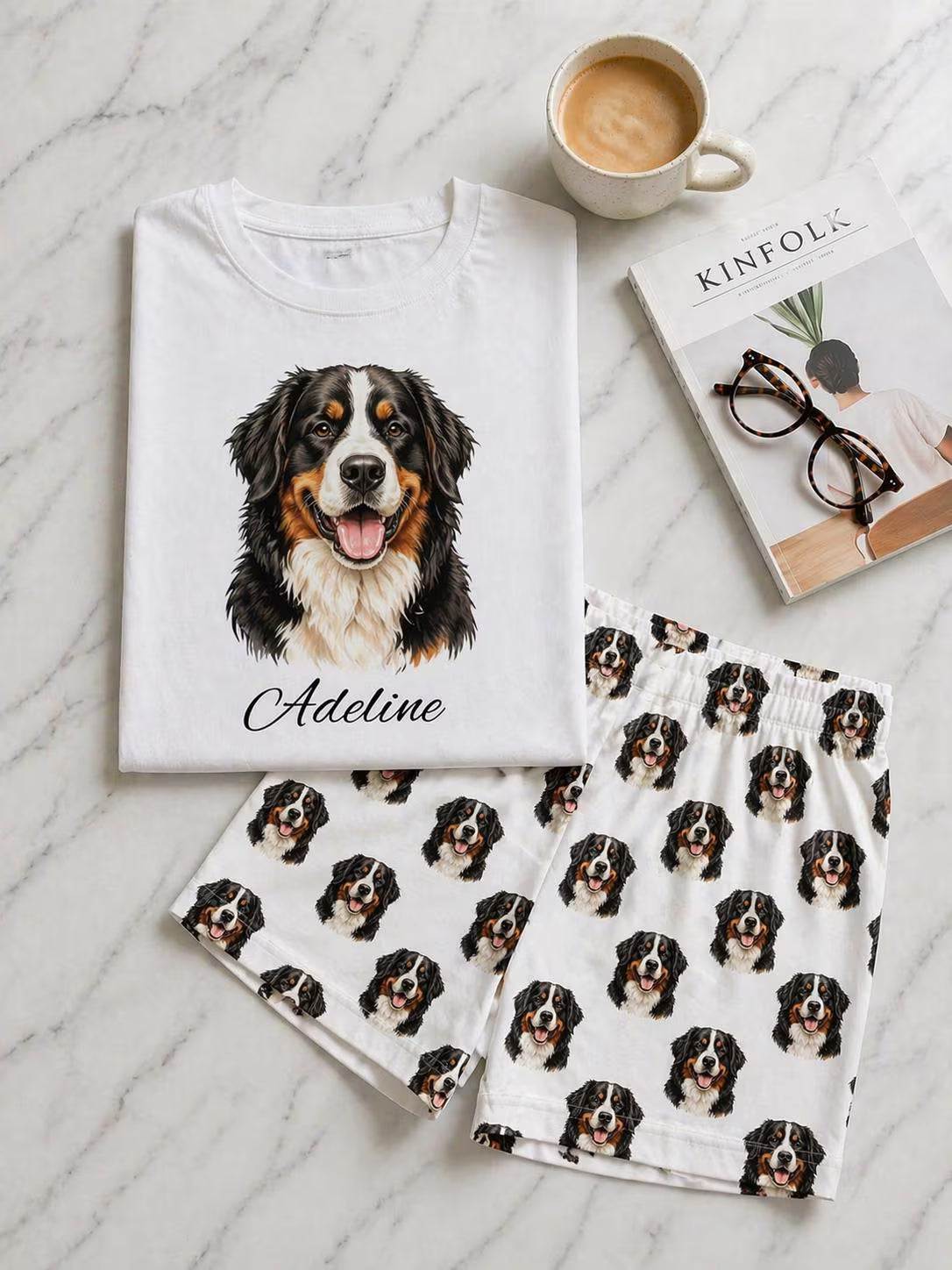 White t-shirt with a dog illustration and name, matching pajama set, and coffee on a marble surface.