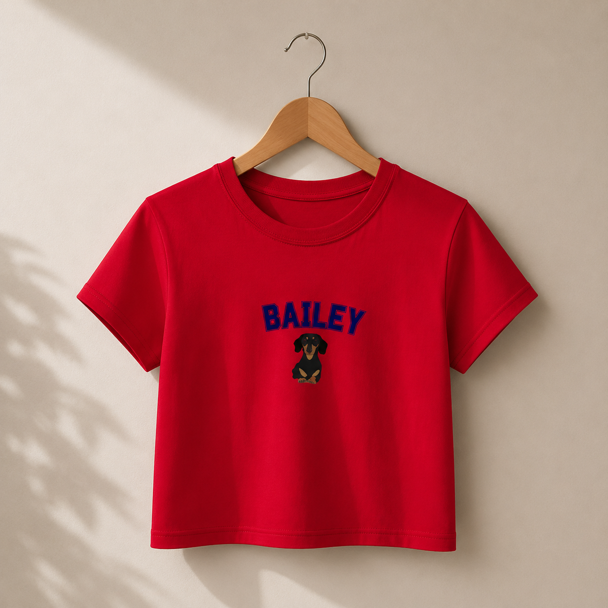 Red t-shirt with 'BAILEY' and a dog graphic on a wooden hanger against a beige background