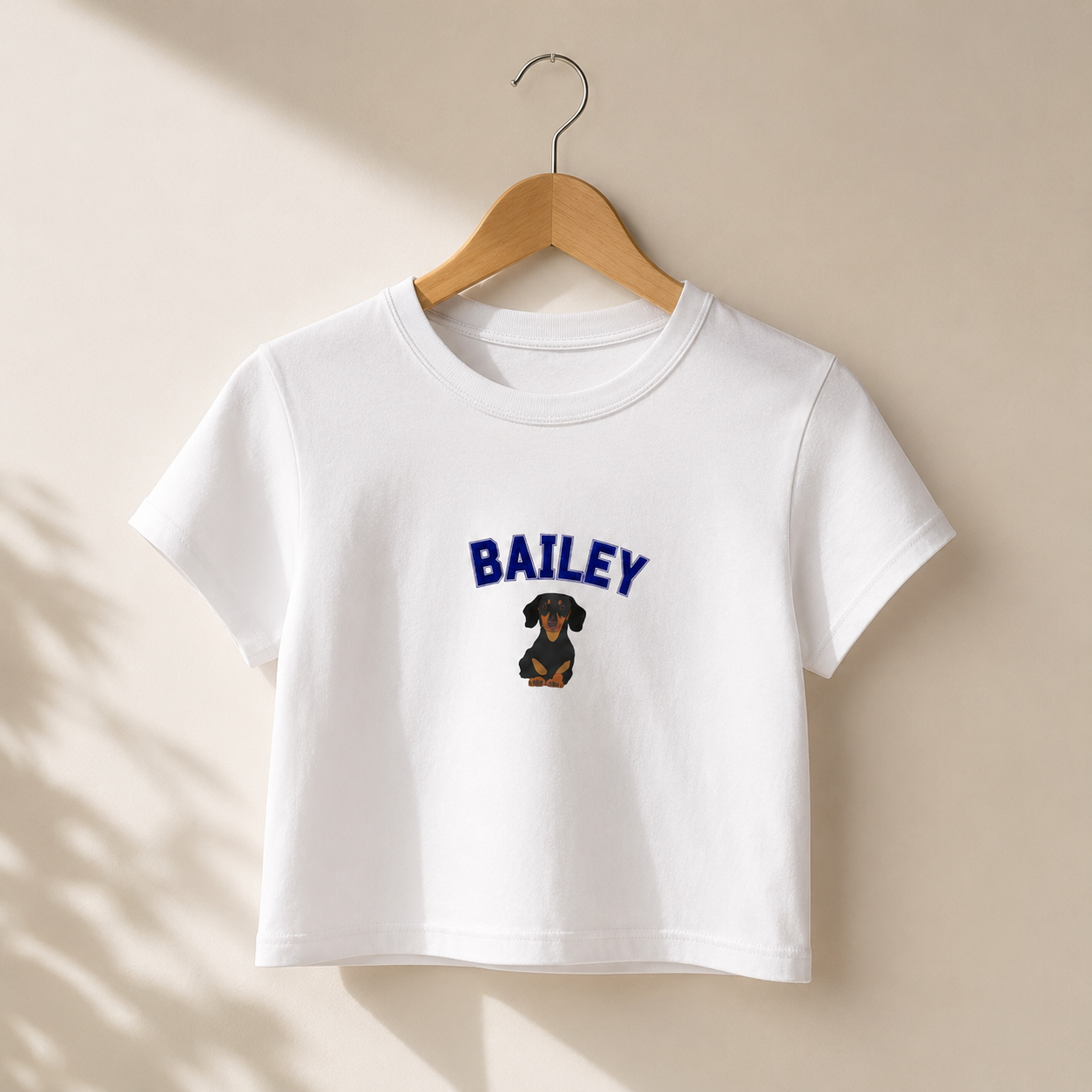 White t-shirt with 'BAILEY' and a dachshund graphic on a beige background